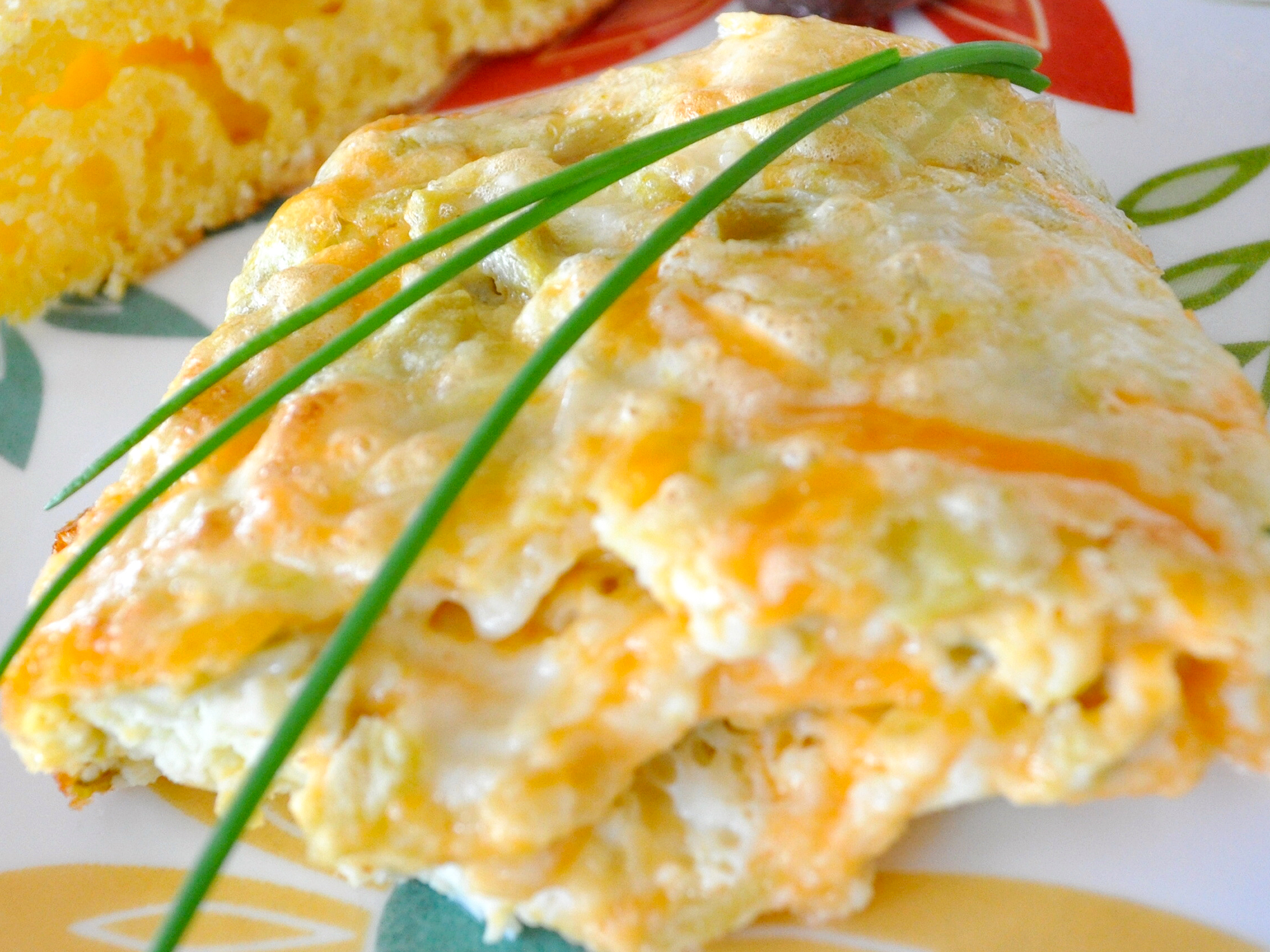 close up view of Green Chile Eggs with cheese, garnished with chives and served with toast on a colorful plate