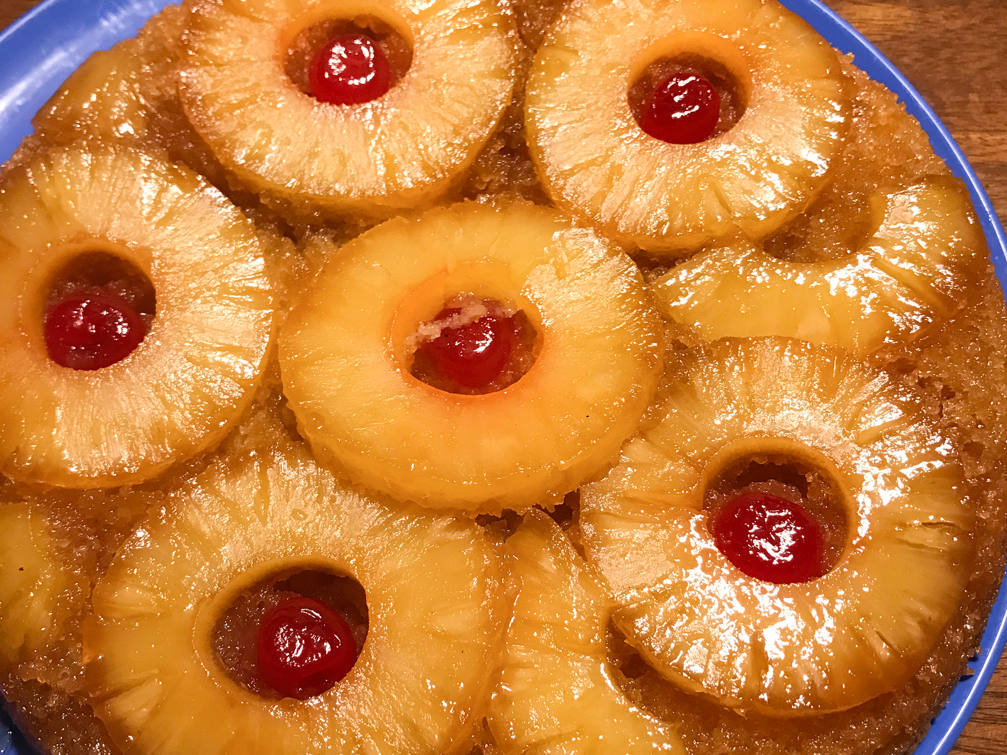 close up view of Pineapple Upside-Down Cake garnished with pineapple slices and Maraschino cherries on a blue plate