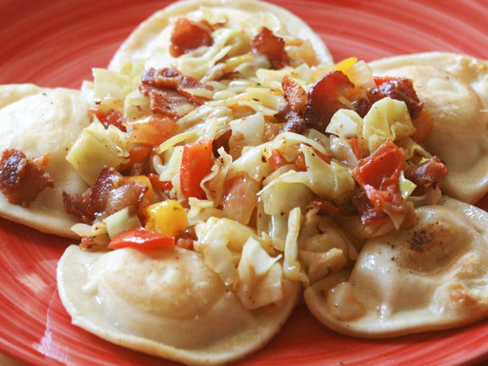 close up view of Pierogies garnished with Cabbage, tomatoes and bacon, on a red plate