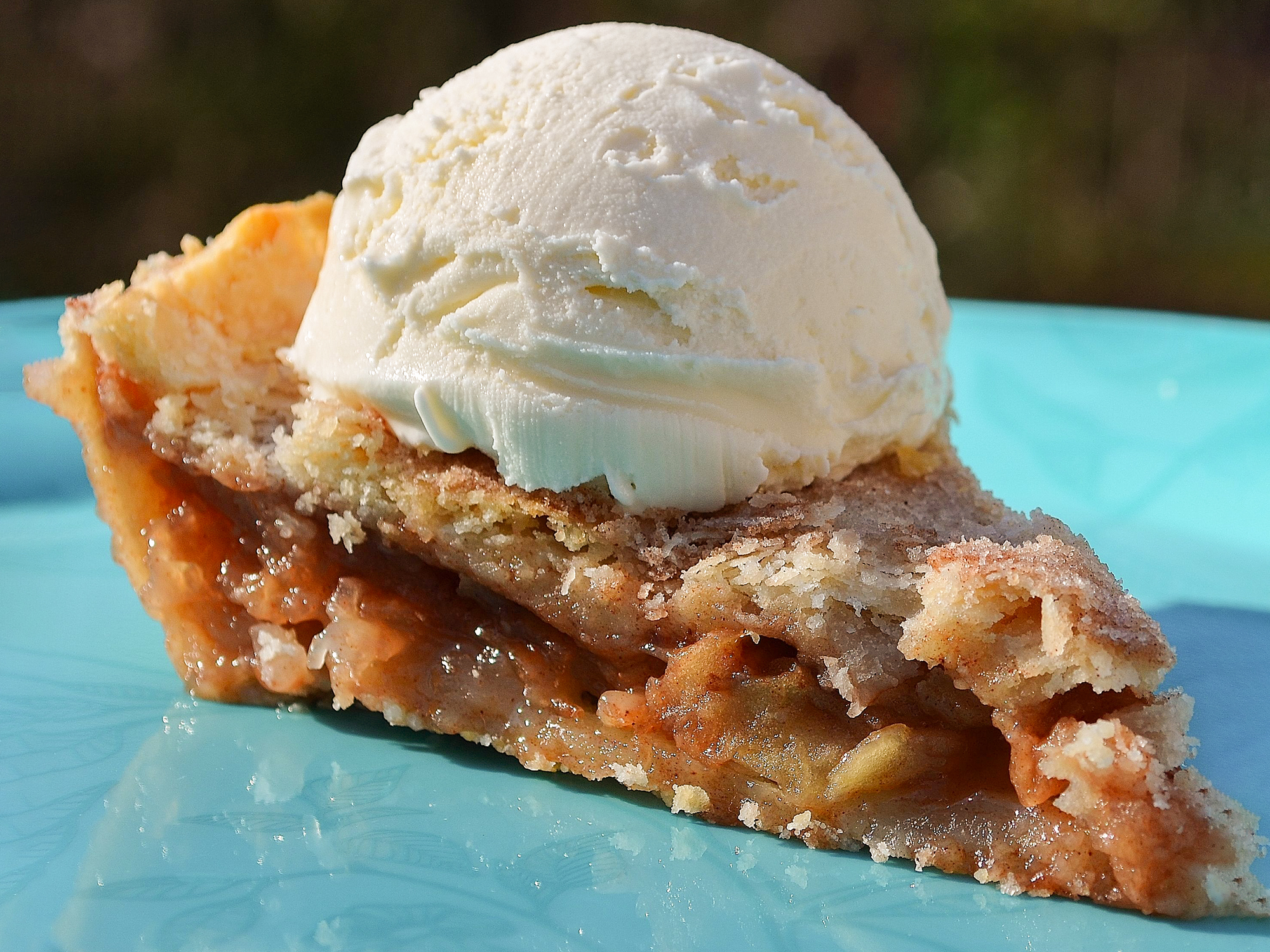 close up view of a slice of Apple Pie with a scoop of vanilla ice cream on top, on a blue plate