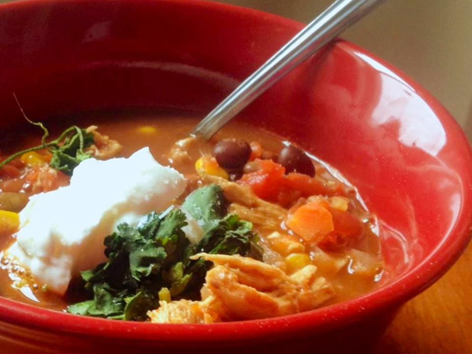 close up view of Slow Cooker Chicken Taco Soup garnished with fresh herbs and sour cream, in a red bowl with a spoon