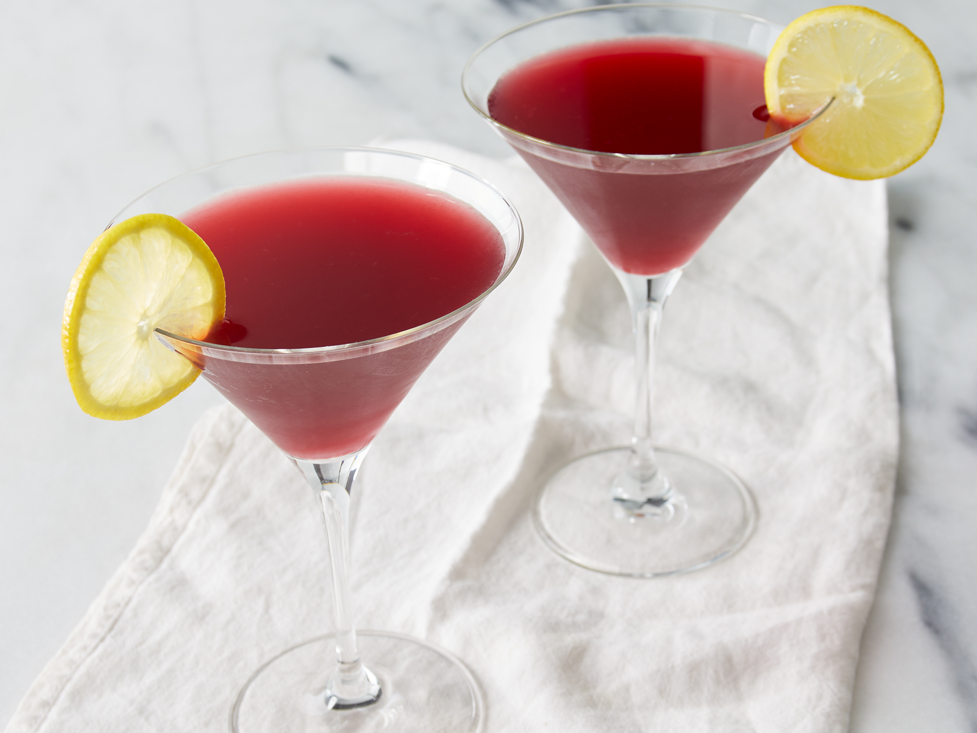 close up on two cosmo-style pomegranate martinis garnished with lemon slices