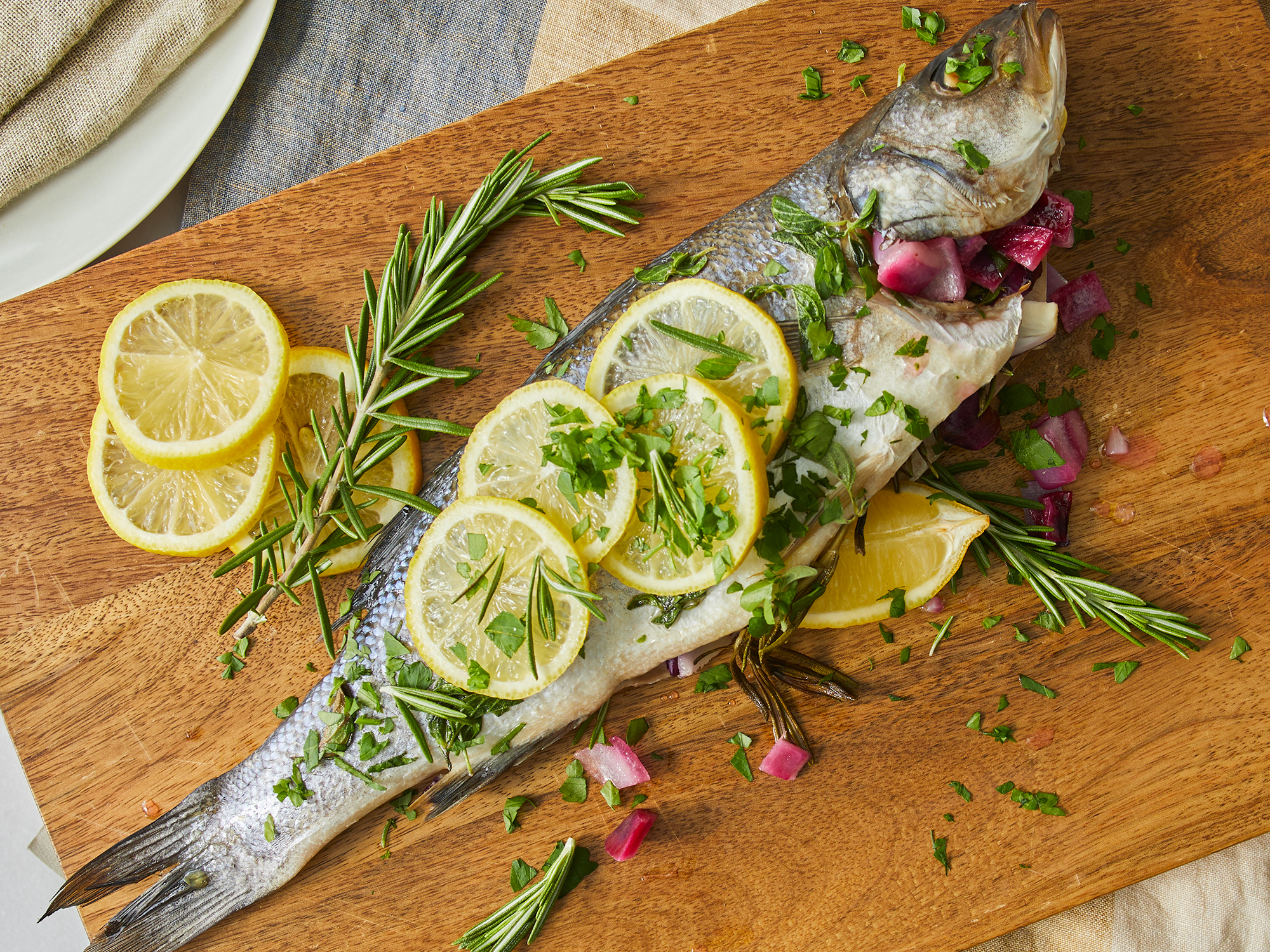 looking down at a cutting board of Branzino Mediterranean garnished with lemon and rosemary