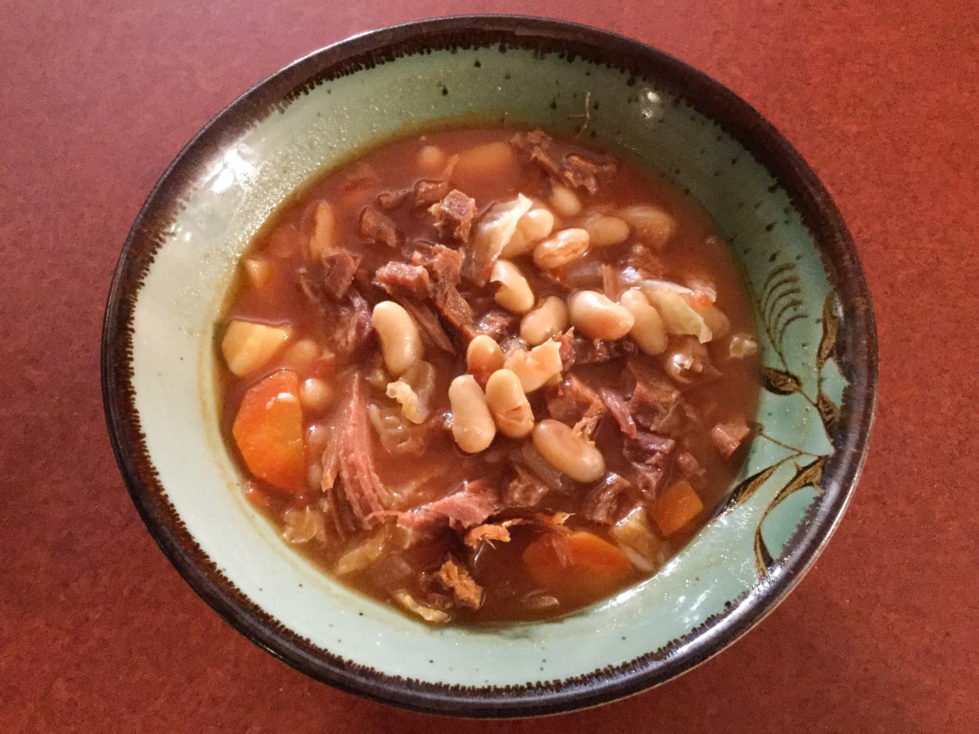 close up view of Ham and Great Northern Bean Soup with carrots and potatoes, in a green bowl