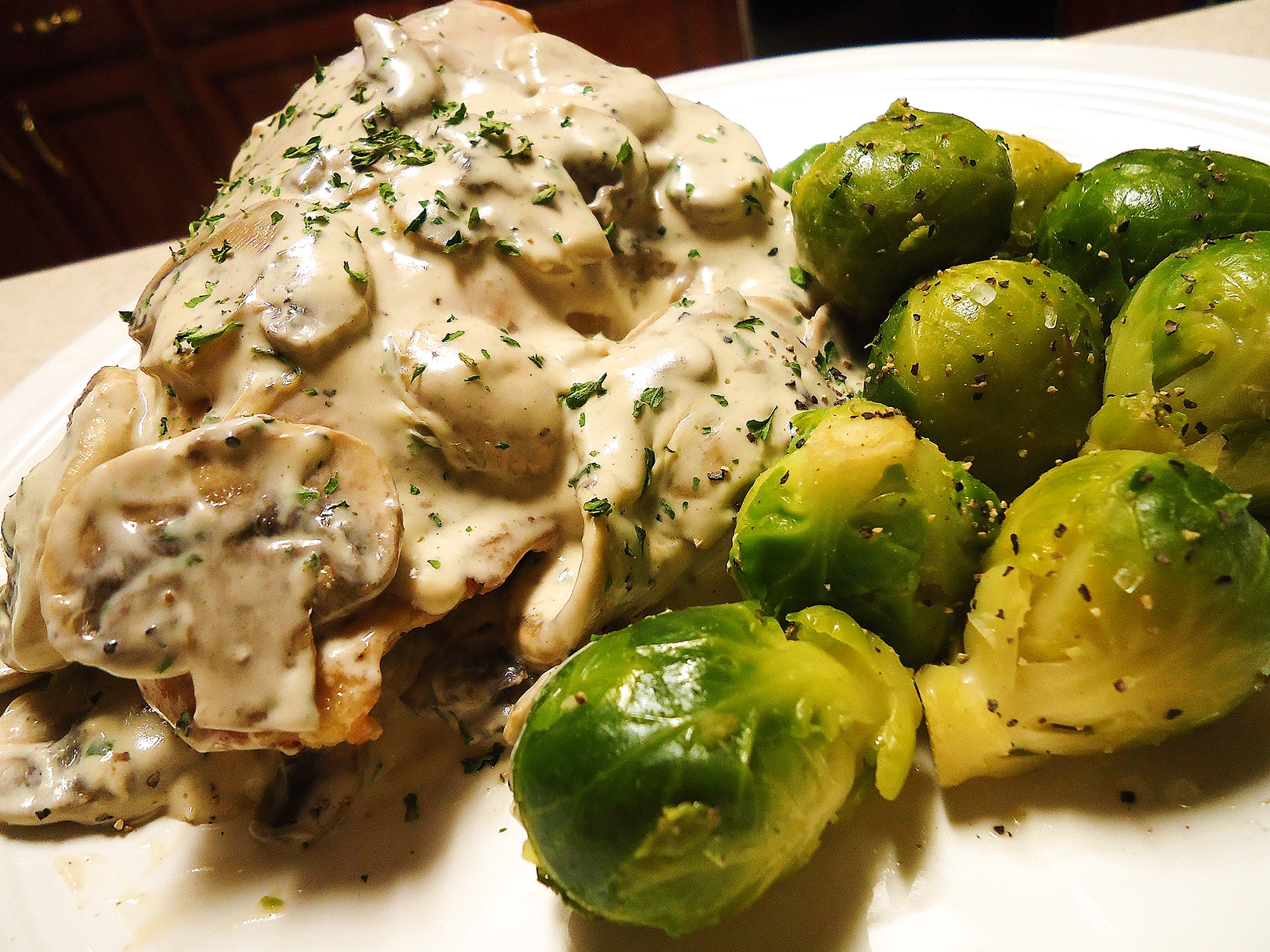 close up view of Mushroom and Swiss Chicken garnished with dry herbs, served with Brussels sprouts, on a white plate