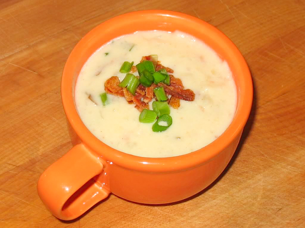 close up view of Cream of Potato Soup garnished with bacon and green onions, in an orange mug