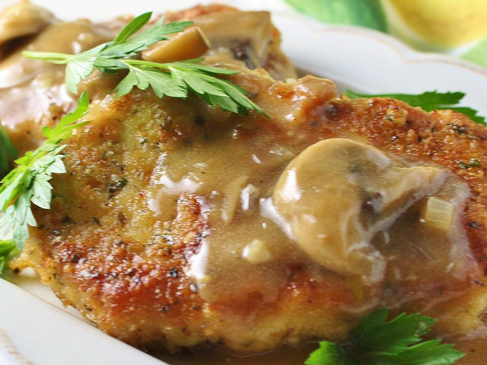 close up view of Butter Schnitzel with mushroom gravy, garnished with fresh herbs, on a white plate