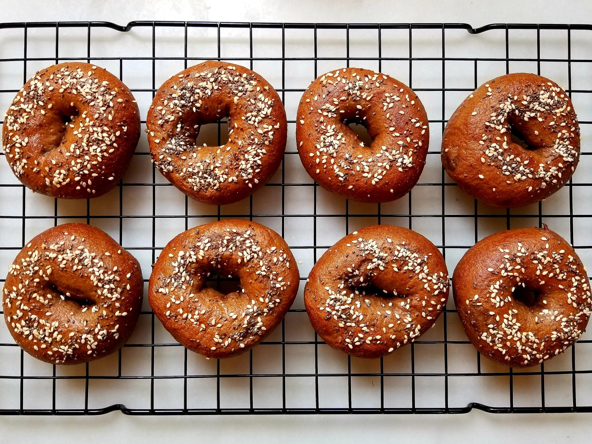 close up view of Pumpernickel Bagels with sesame seeds and chia seeds on top, on a cooling rack