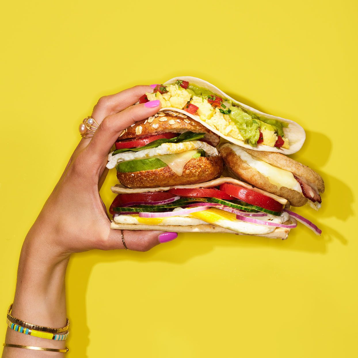 hand holding several precariously stacked breakfast sandwiches