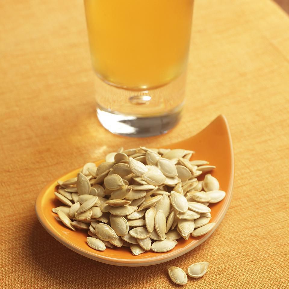 bowl of roasted pumpkin seeds in an orange bowl next to a pint of beer