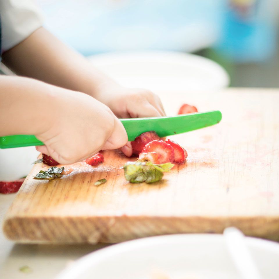 Child cutting strawberries with plastic knife