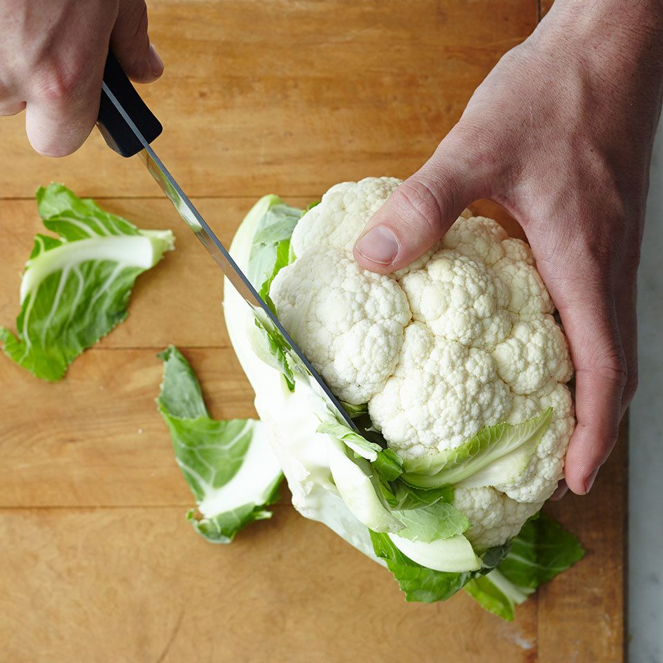 removing the leaves from cauliflower with a knife