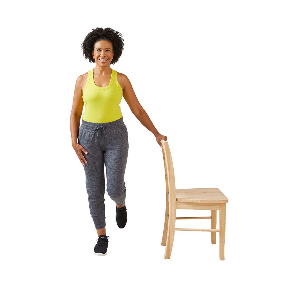woman with hand on chair doing single leg balance