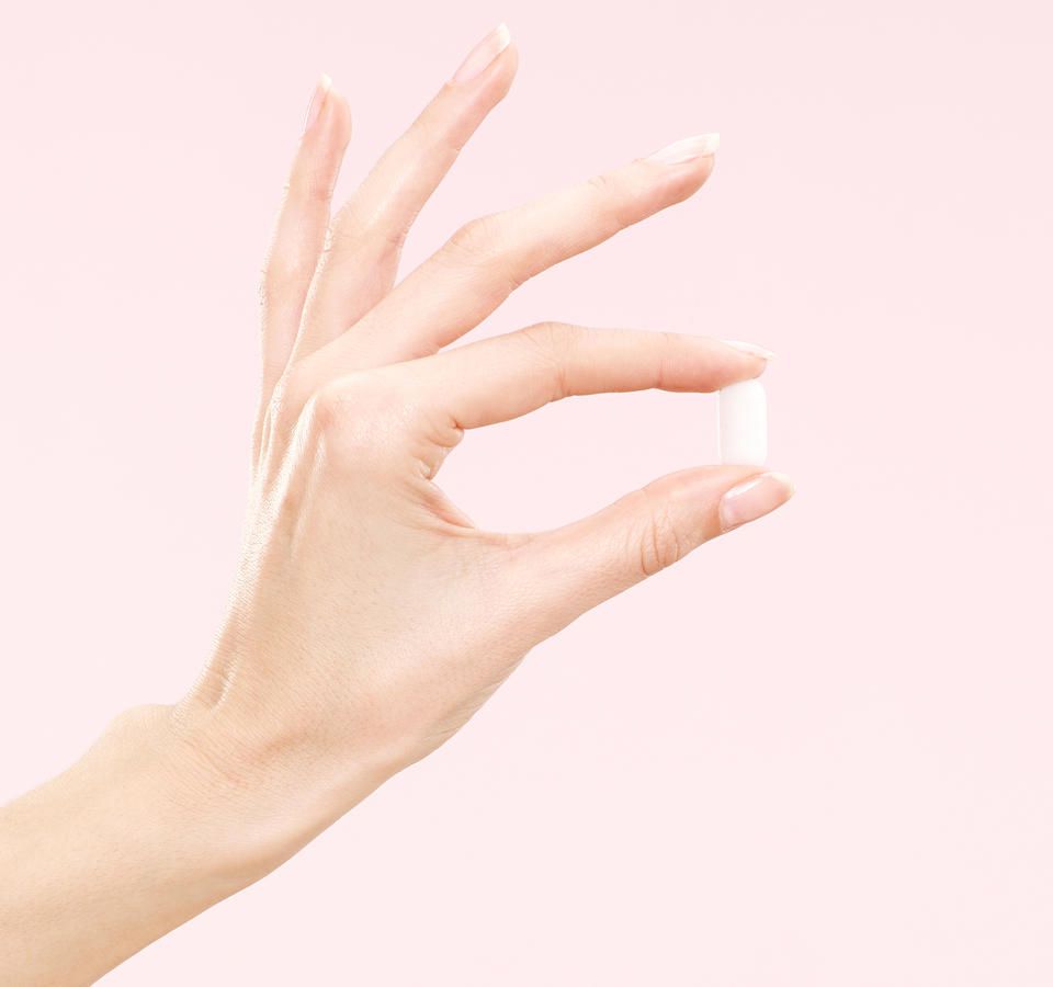 woman's thumb and index finger holding white pill with pink background