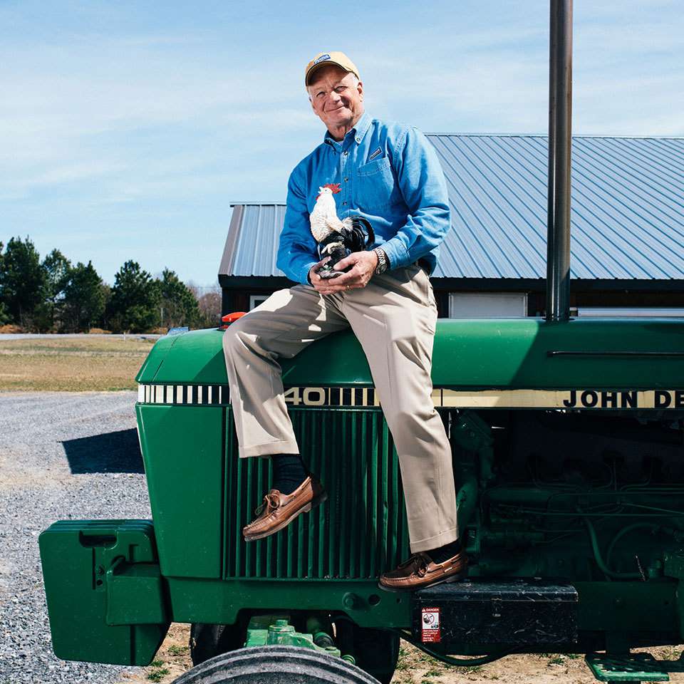Jim Perdue sits on a green tractor holding a chicken statue