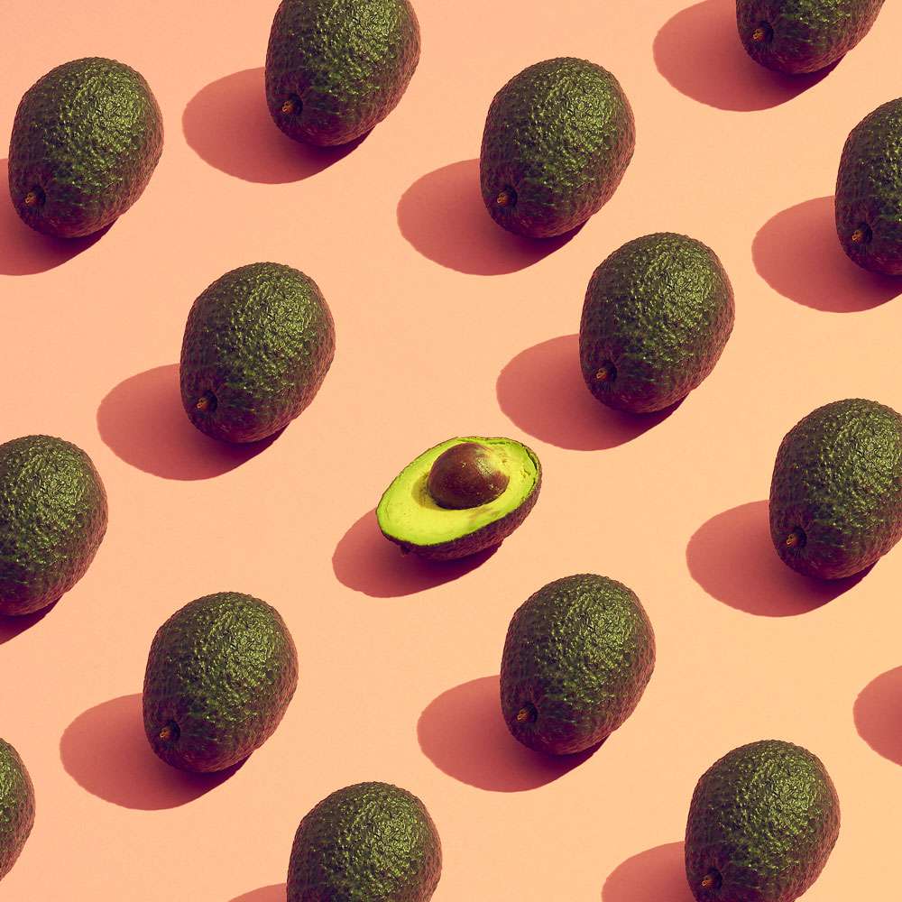 whole avocados neatly placed on a surface with one cut open in the middle
