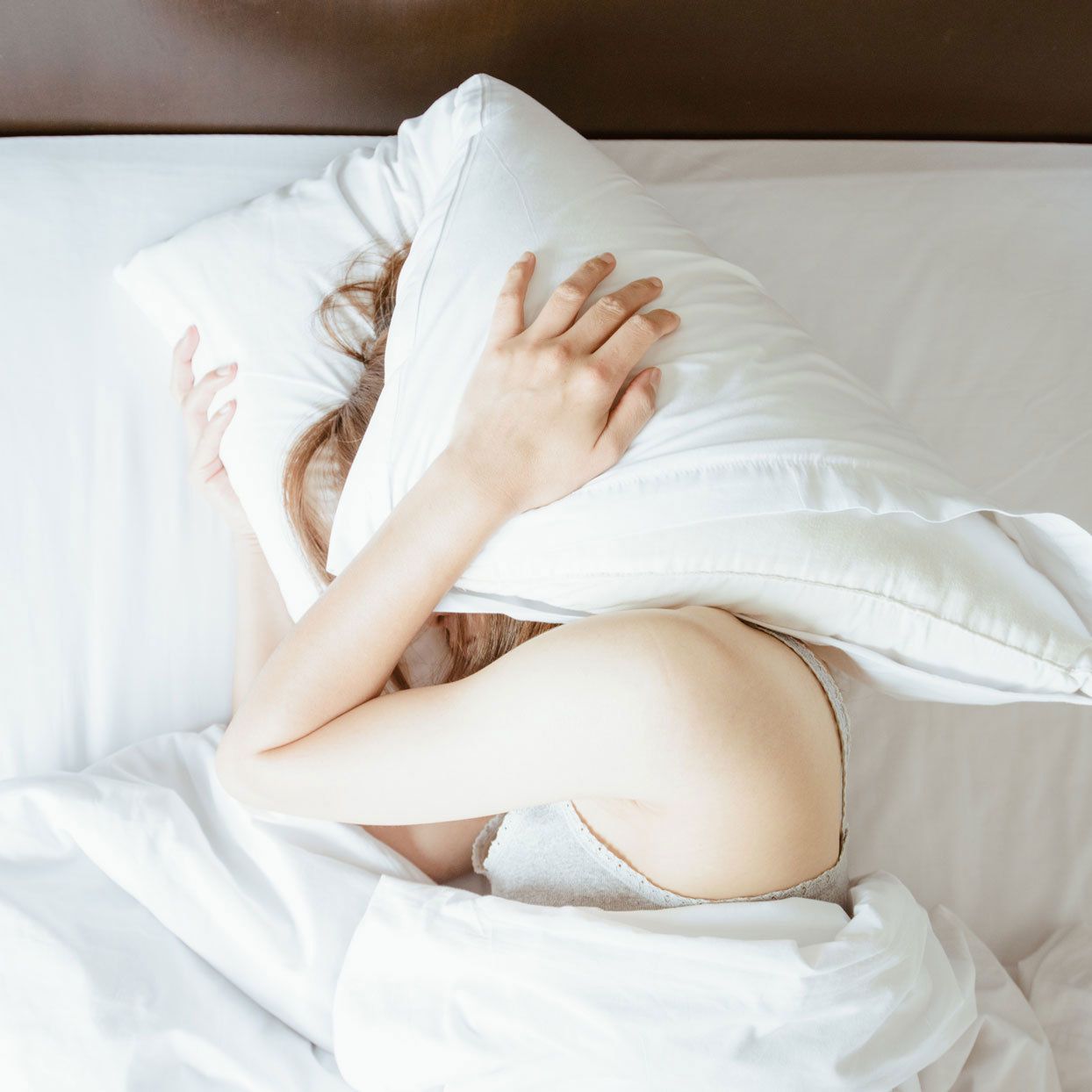 woman laying in bed and holding a pillow over her head