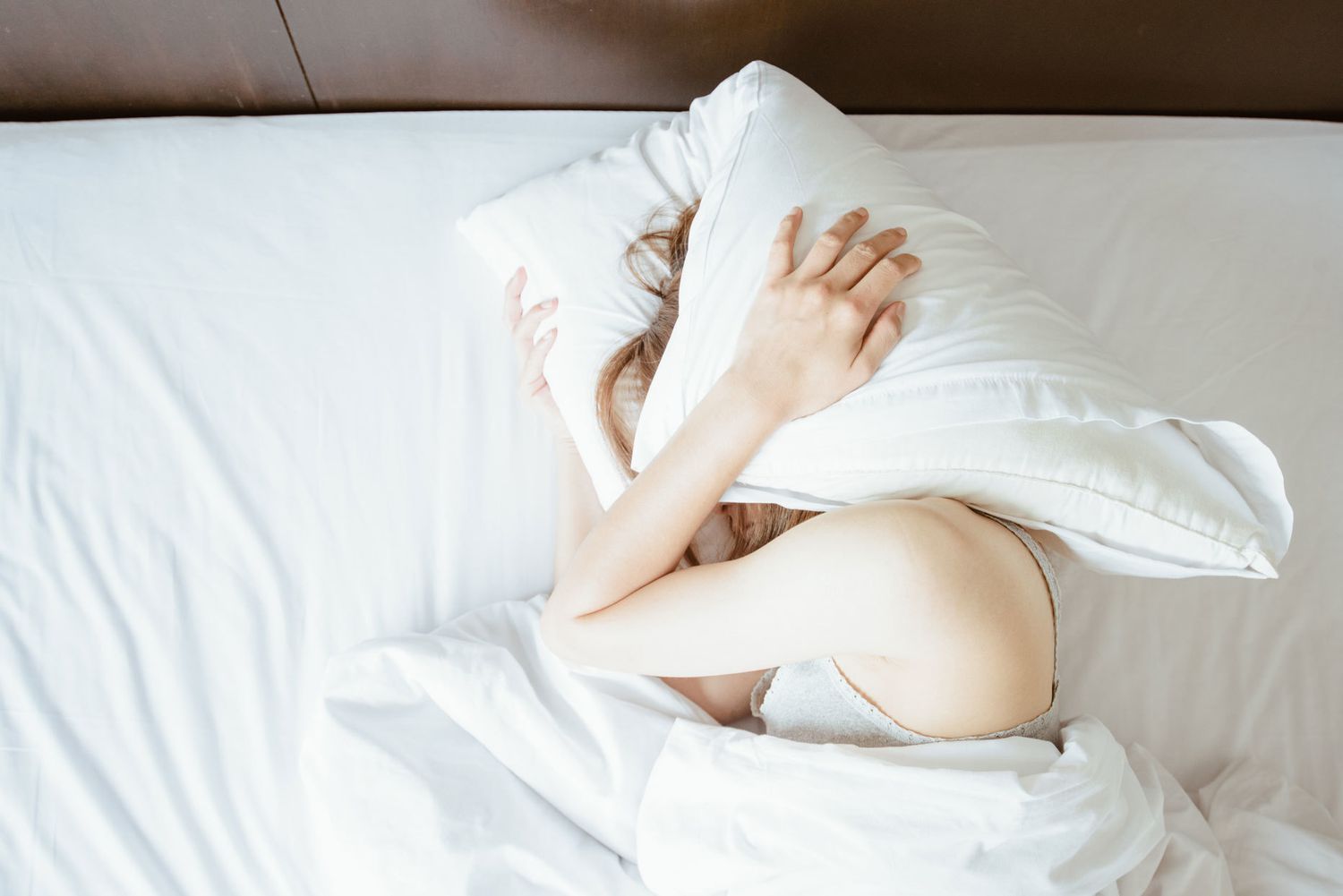 woman laying in bed and holding a pillow over her head