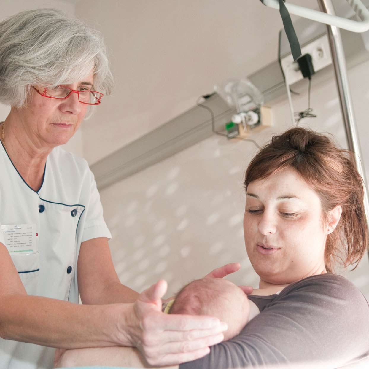 new mother holding a newborn with a nurse helping