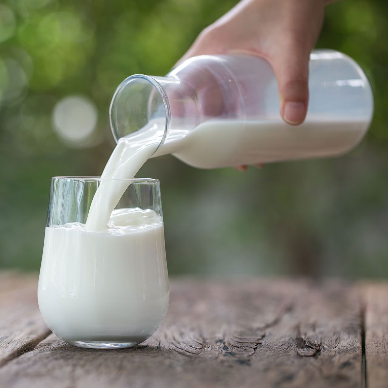 Someone pouring milk into a glass from a glass milk jug
