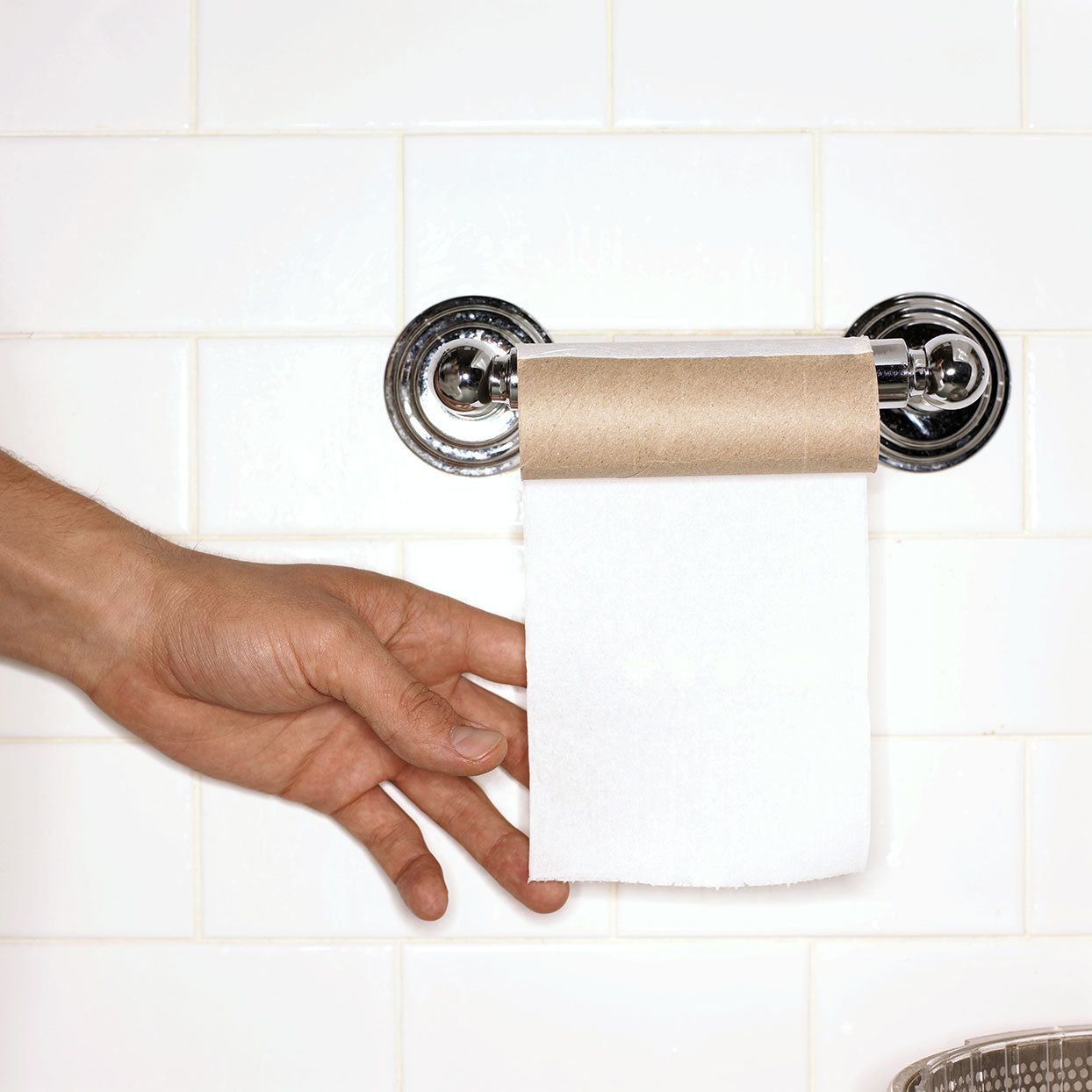 A hand reaches for the last piece of toilet paper on roll