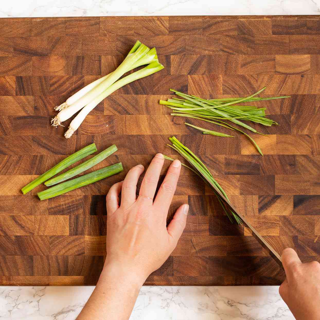 cutting green onions lengthwise on a wooden cutting board