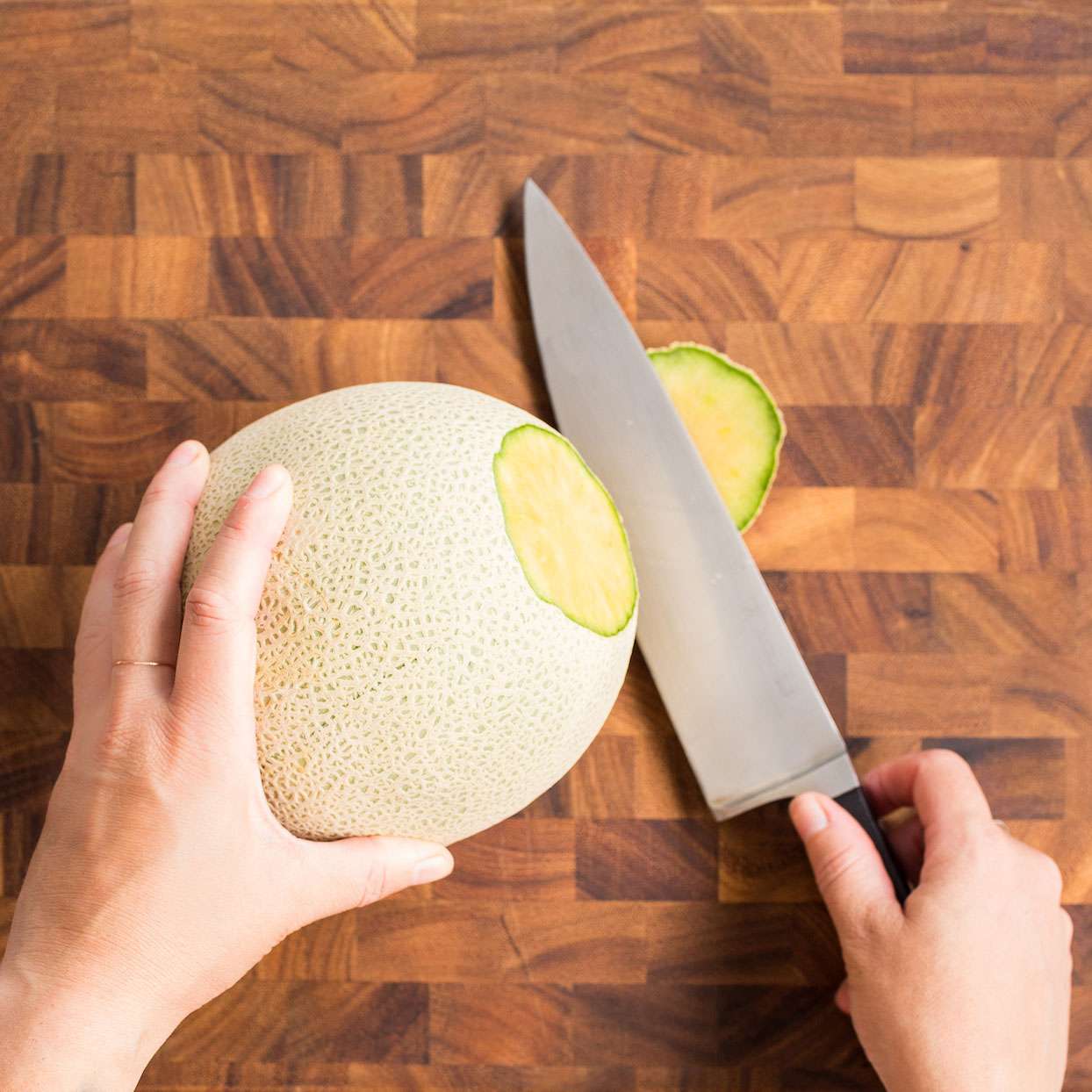 knife slicing top of cantaloupe on wooden cutting board