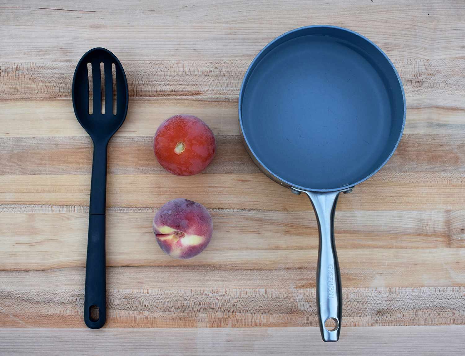 tomato, peach, slotted spoon and pot of water on a cutting board.