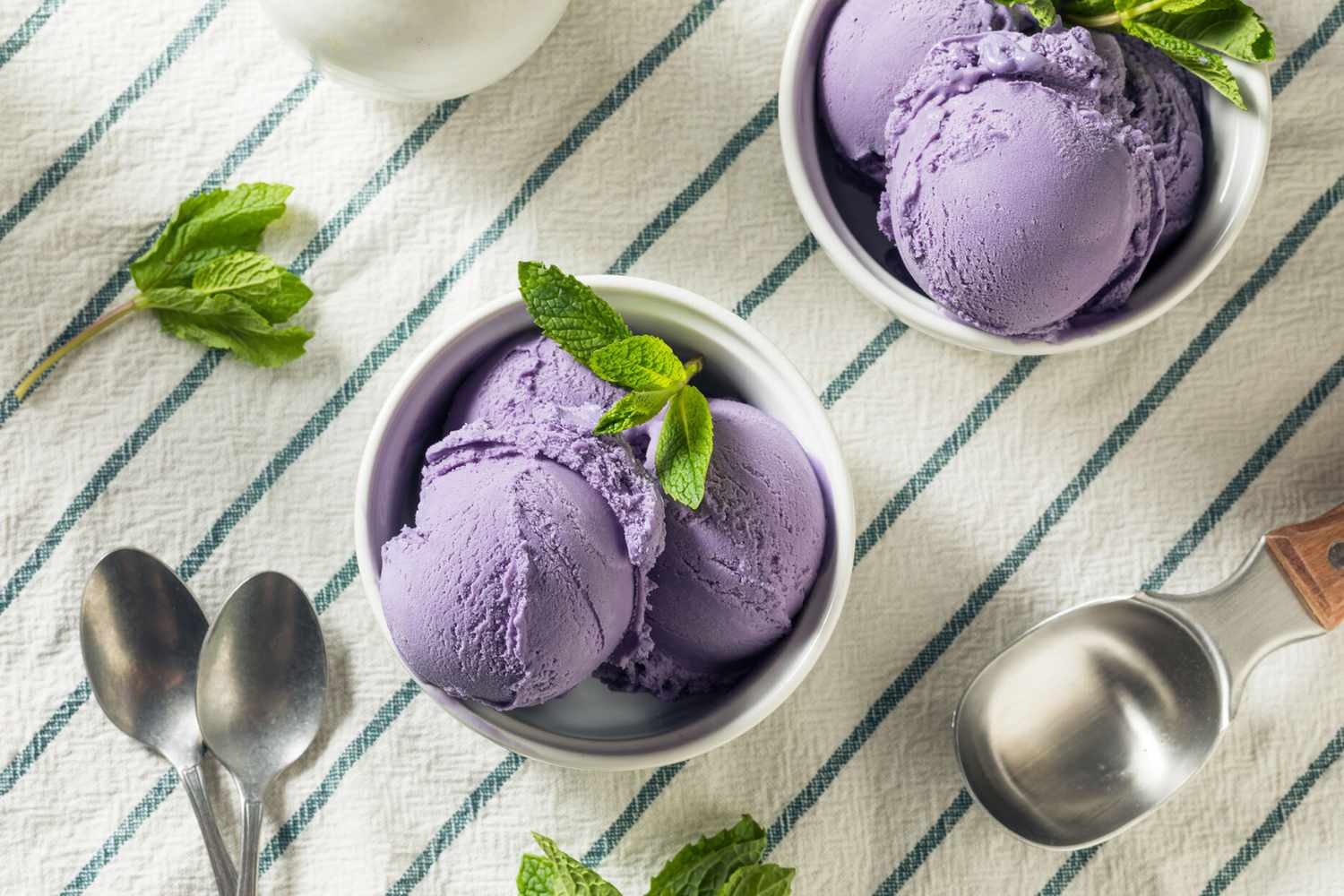 Ube ice cream in bowls on a table with a scoop and spoons