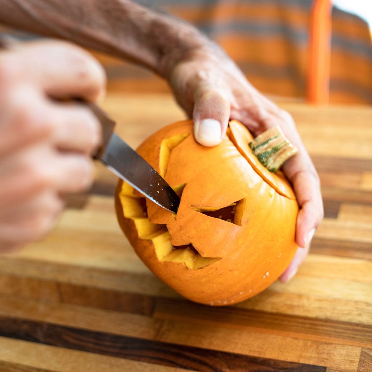 person carving pumpkin with a kitchen knife