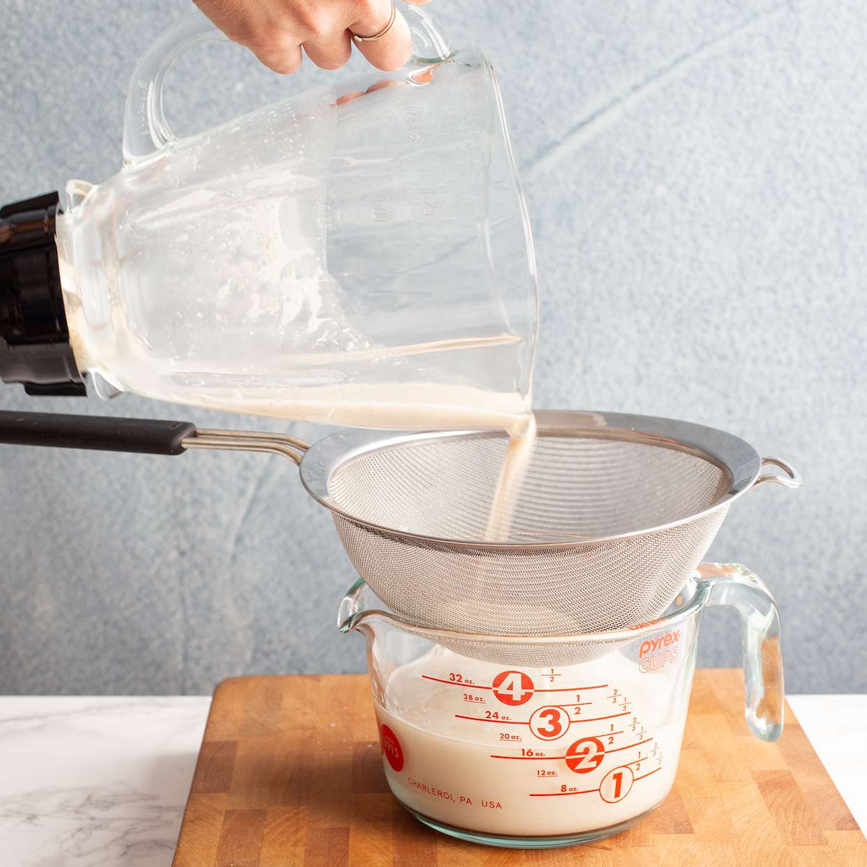 Pouring oat milk from blender through fine-mesh strainer