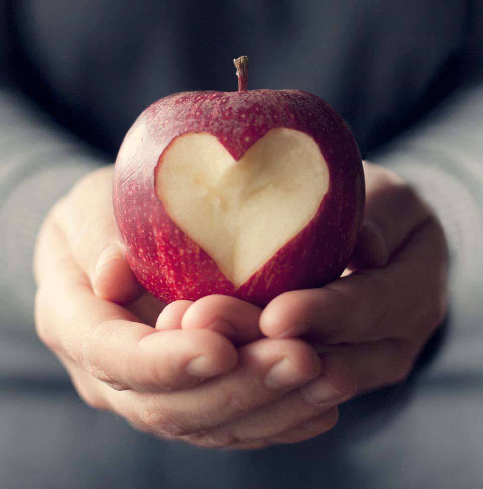 Hands holding a red apple with a heart shape carved out of it