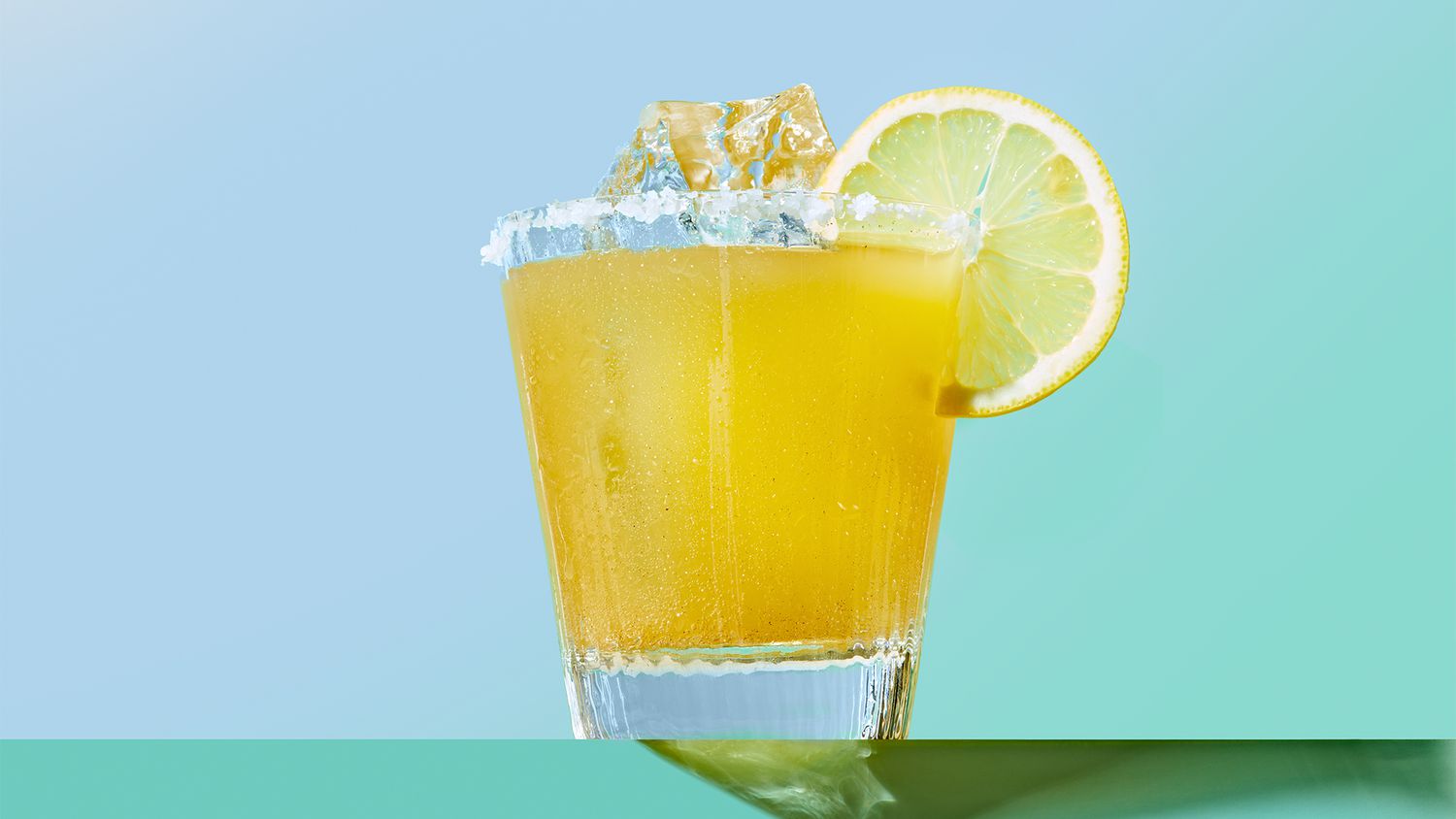 a photograph of a yellow cocktail with a blue background