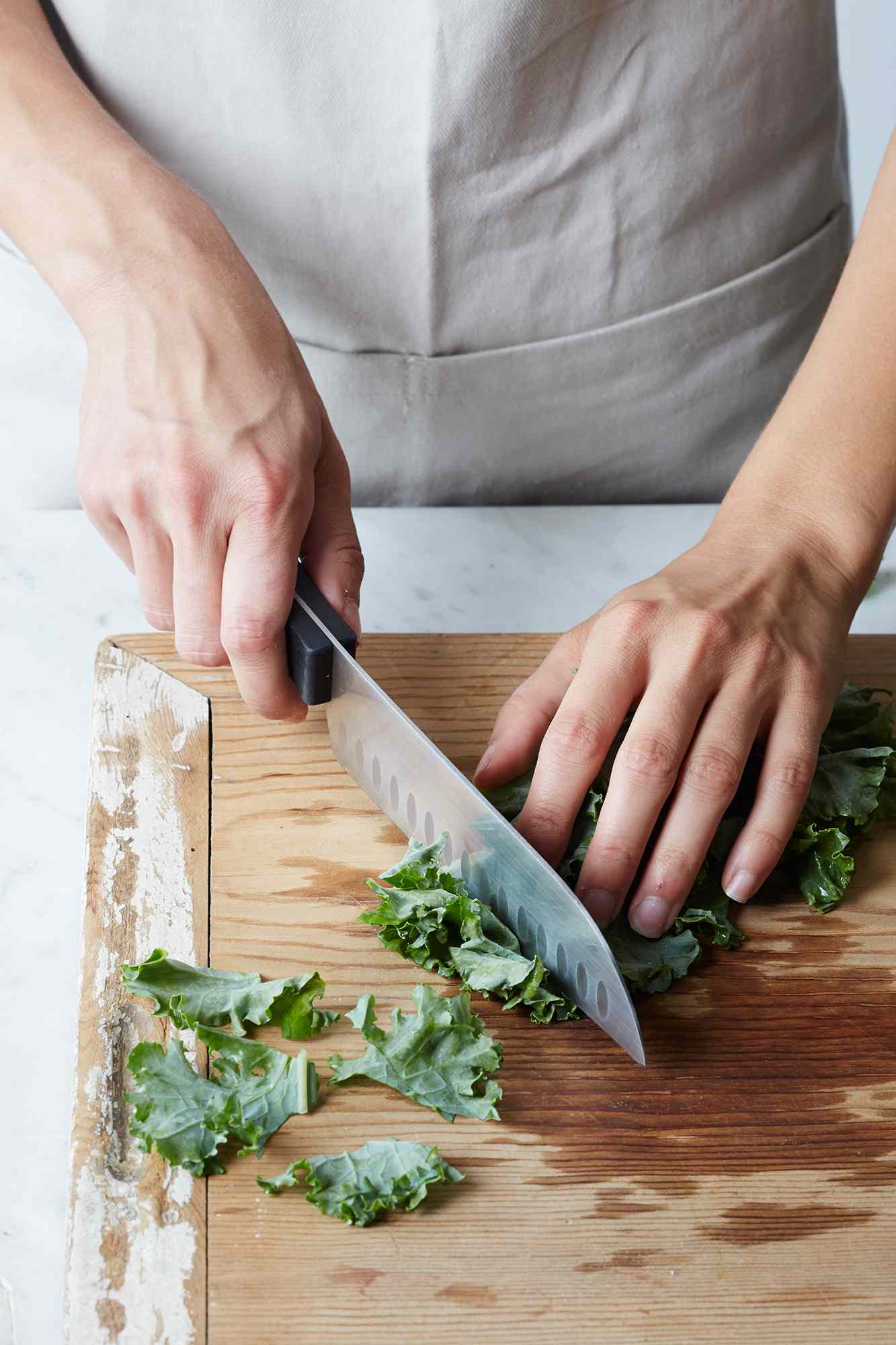 A close up of hands using a knife to cut kale on a cutting board