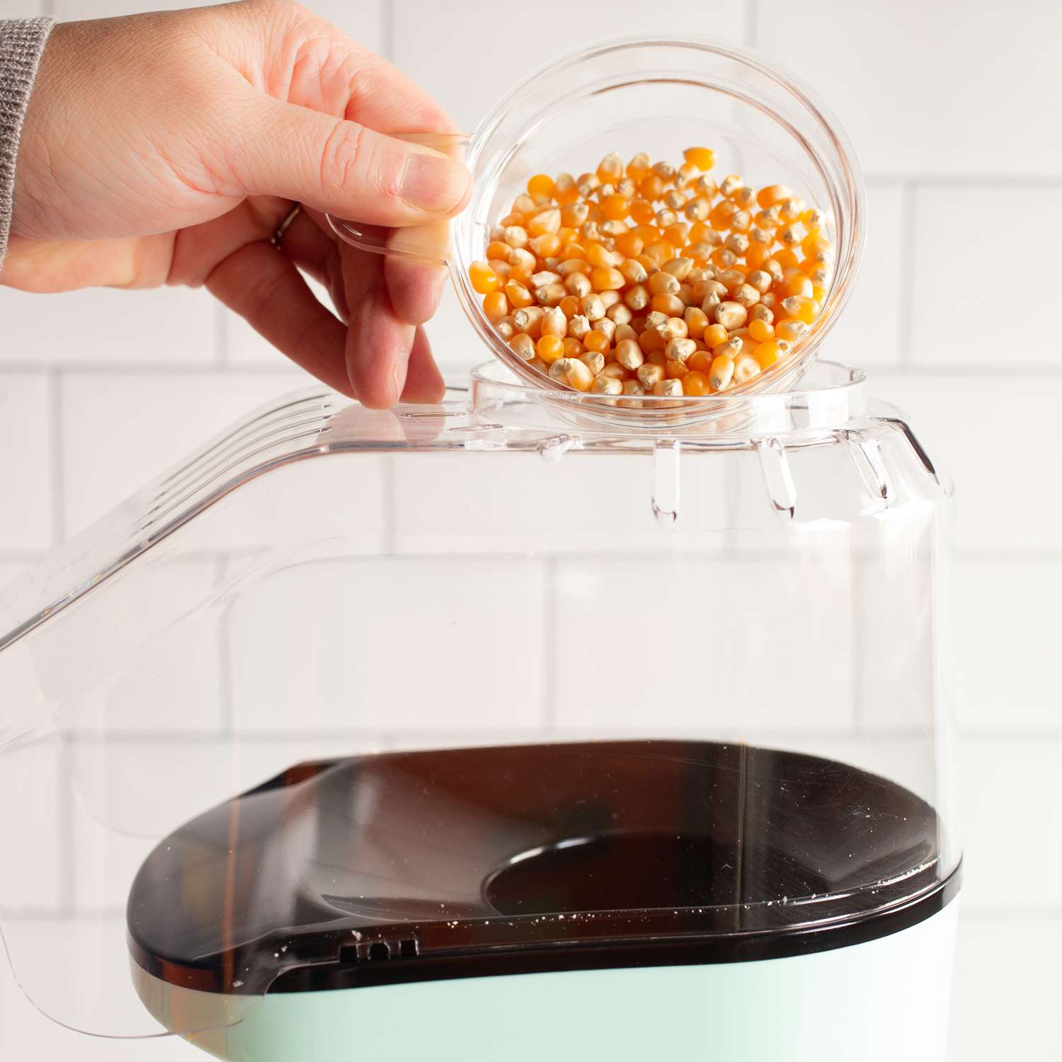 A close up of a hand pouring popcorn kernels into an air popper