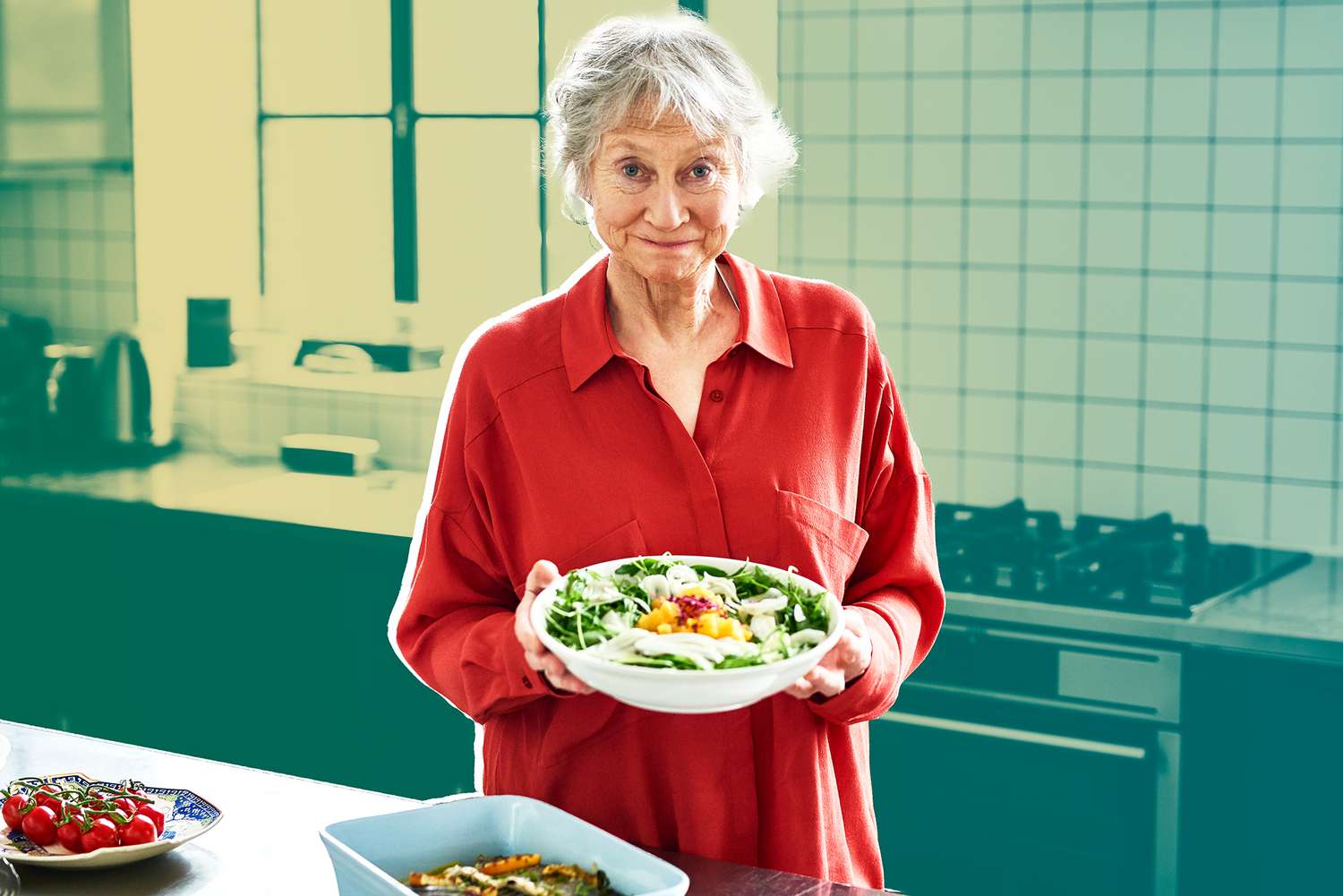 Cheerful senior woman holding fresh salad in modern kitchen