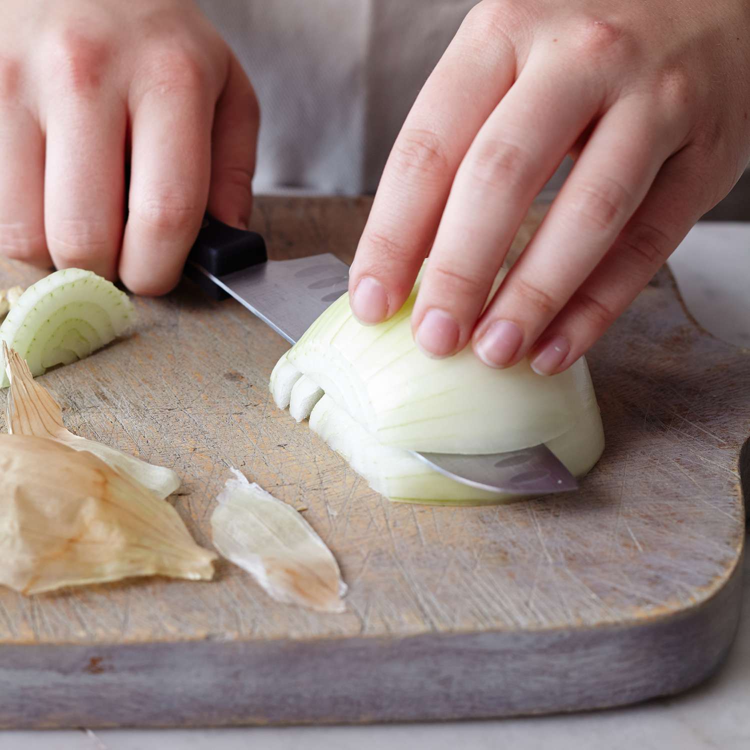 Midsection of woman chopping white onion on wooden board at table