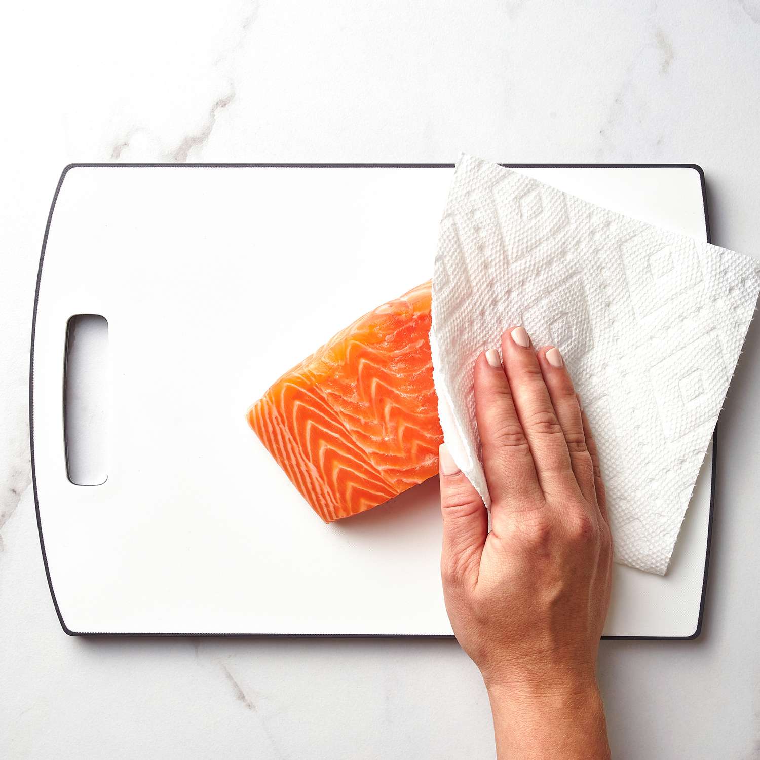 A hand patting down a piece of salmon with a paper towel