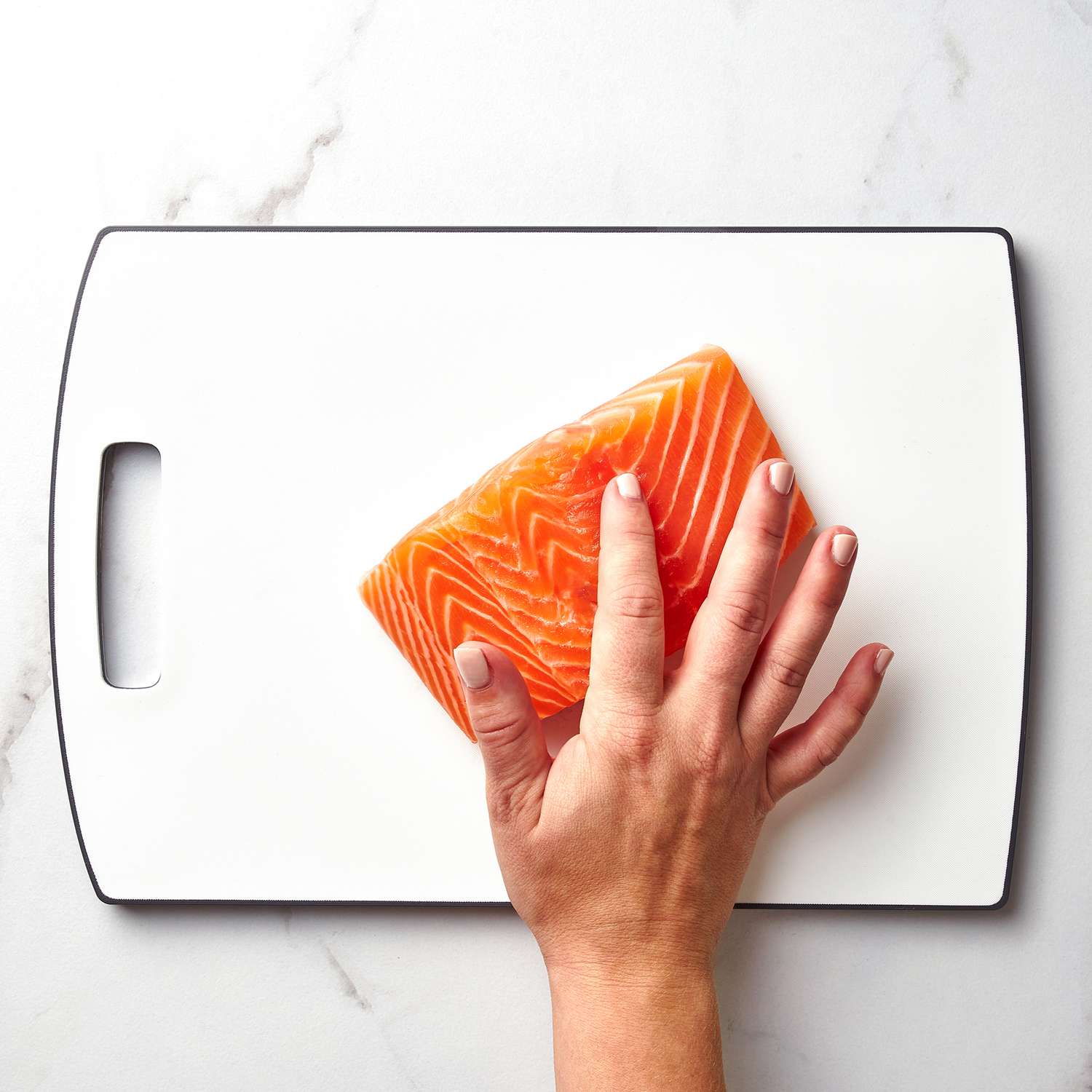 A hand running over salmon on a white cutting board
