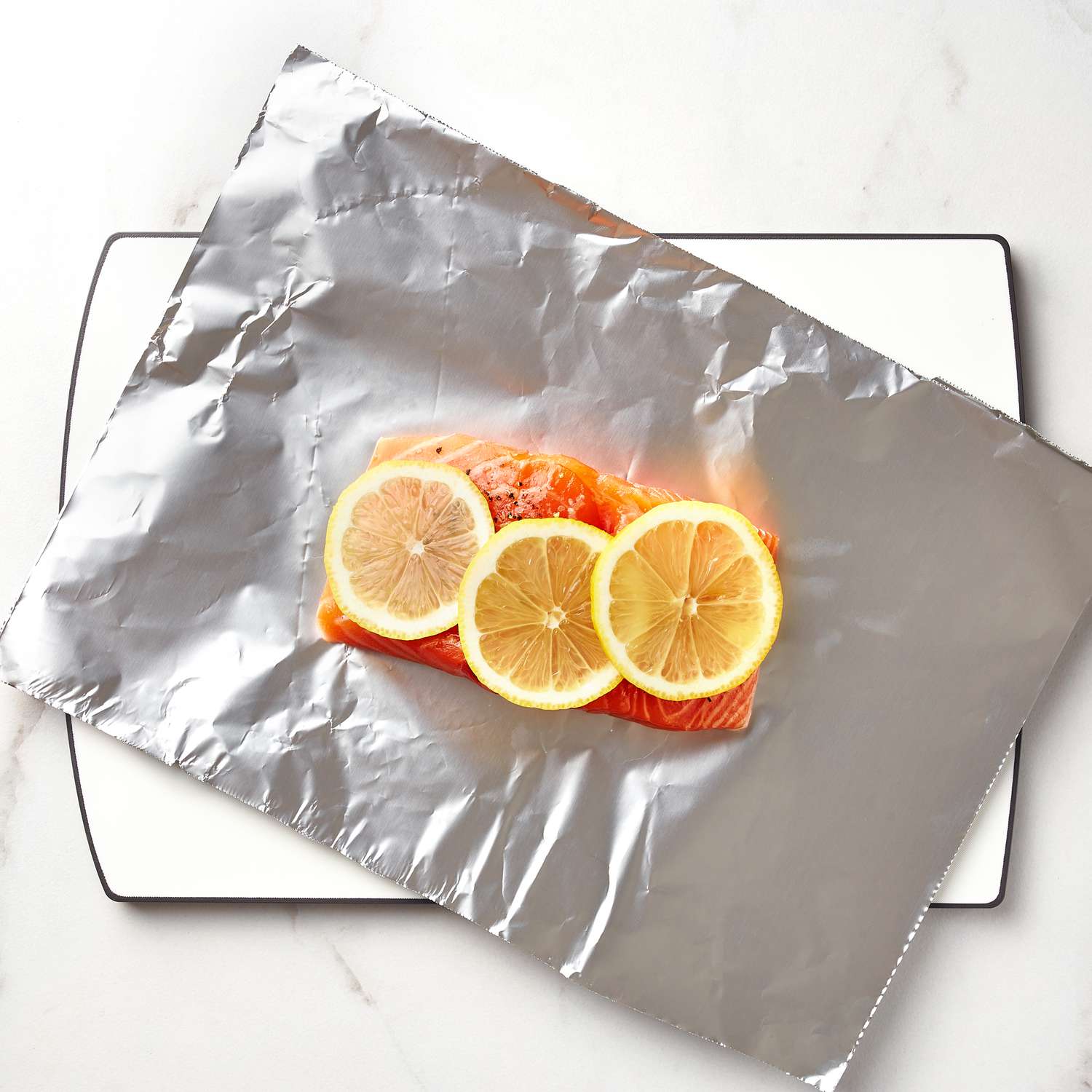 salmon fillet covered in lemon wedges on a tin foil sheet