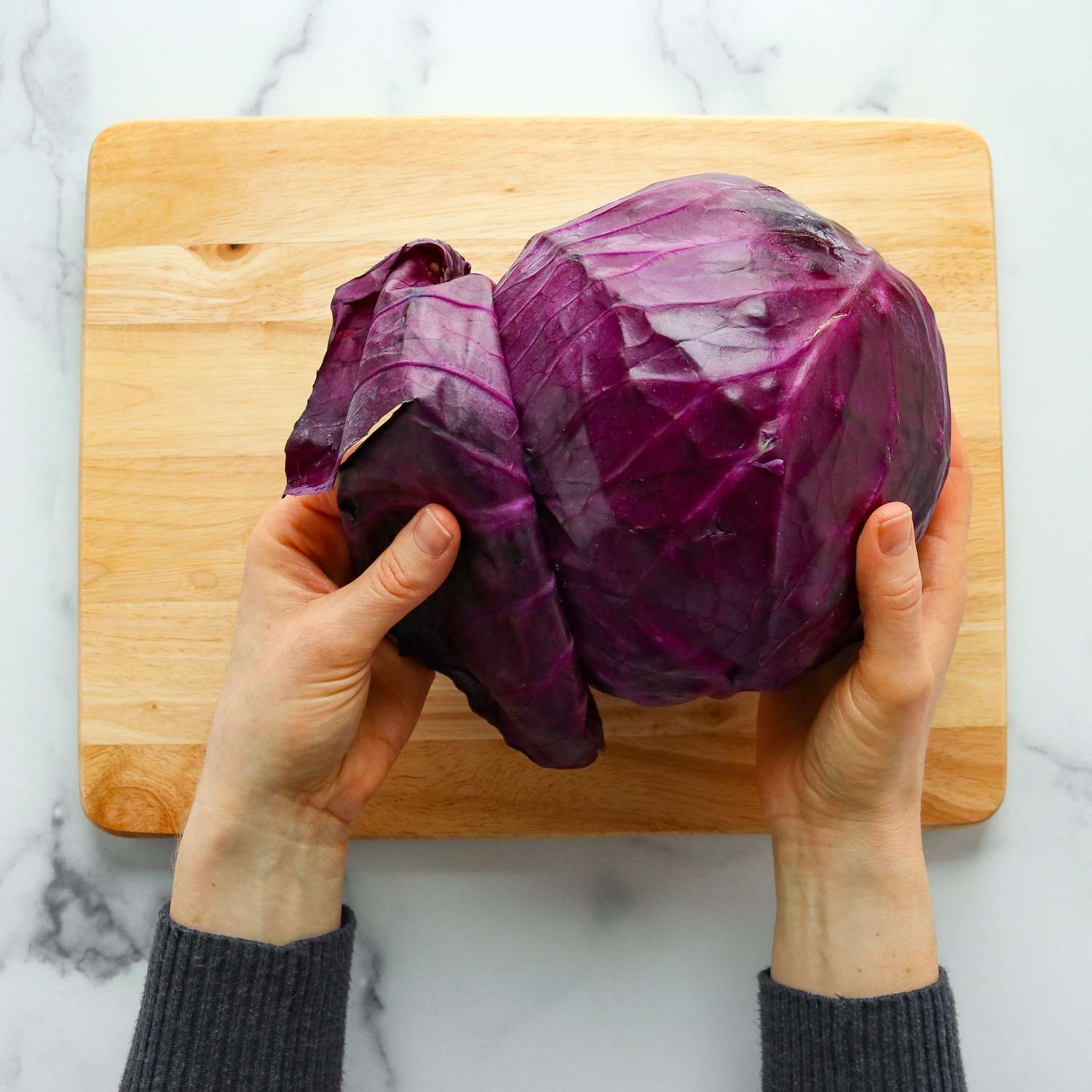 Hands peeling leaves off a head of purple cabbage
