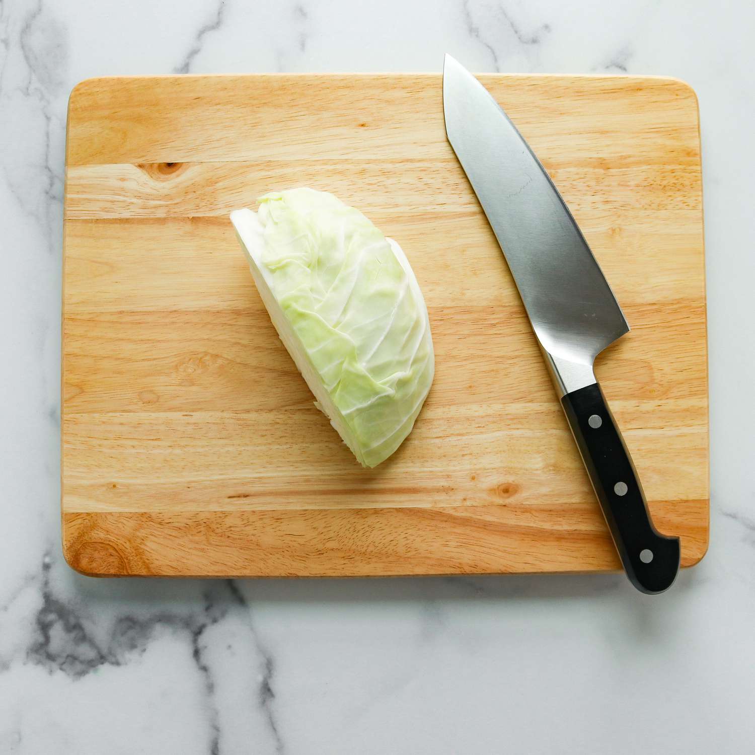 A wedge of cabbage sitting on a cutting board next to a knife