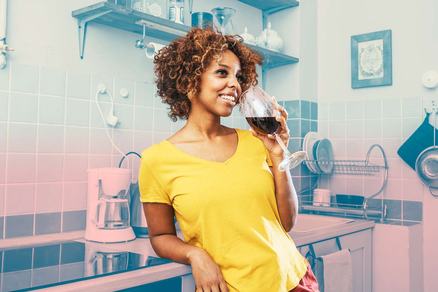 Smiling young woman drinking glass of red wine in kitchen