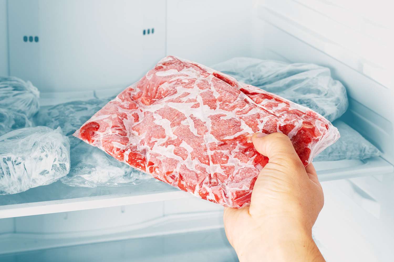 hand taking out frozen meat from freezer.