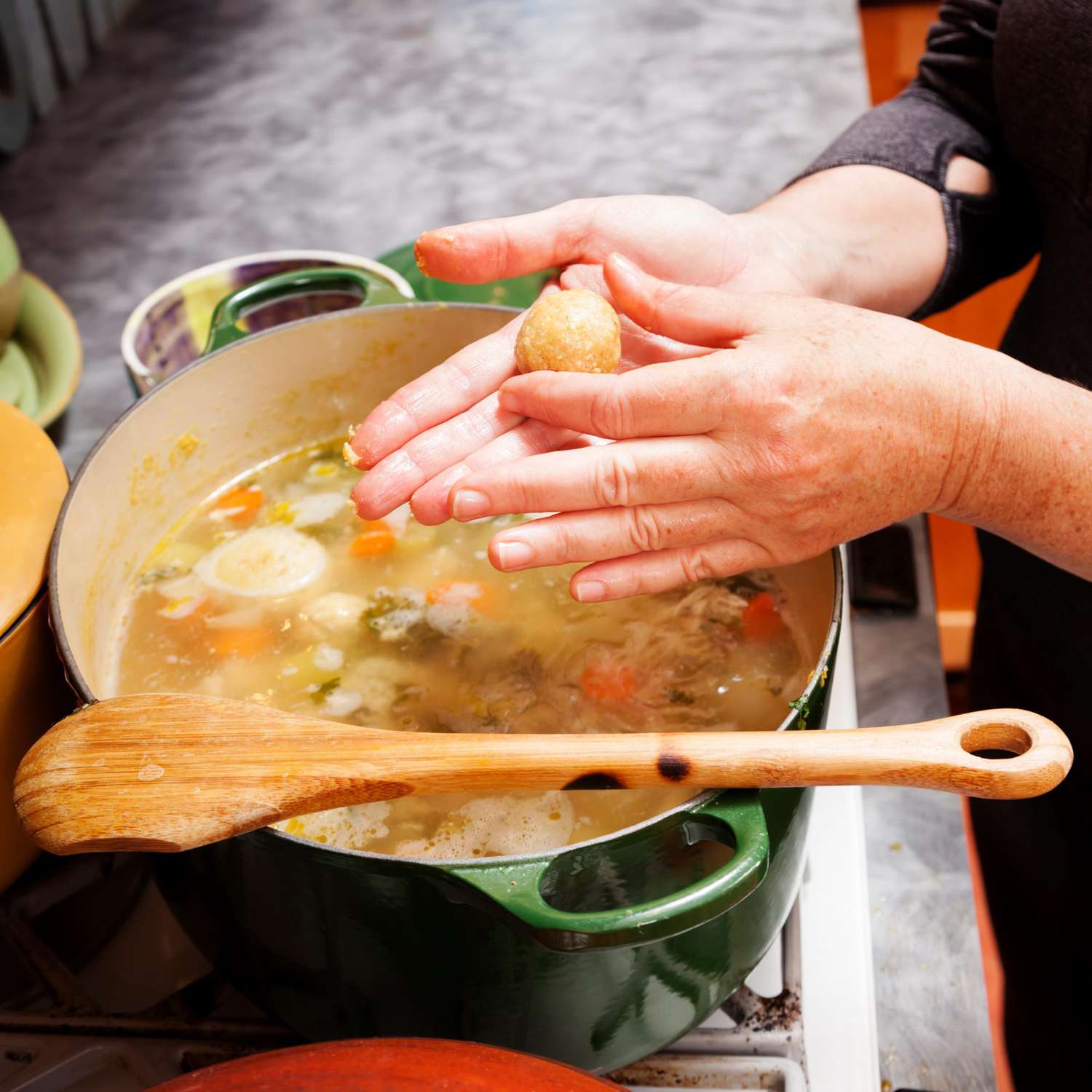 Hands forming a matzoh ball over a pot of soup