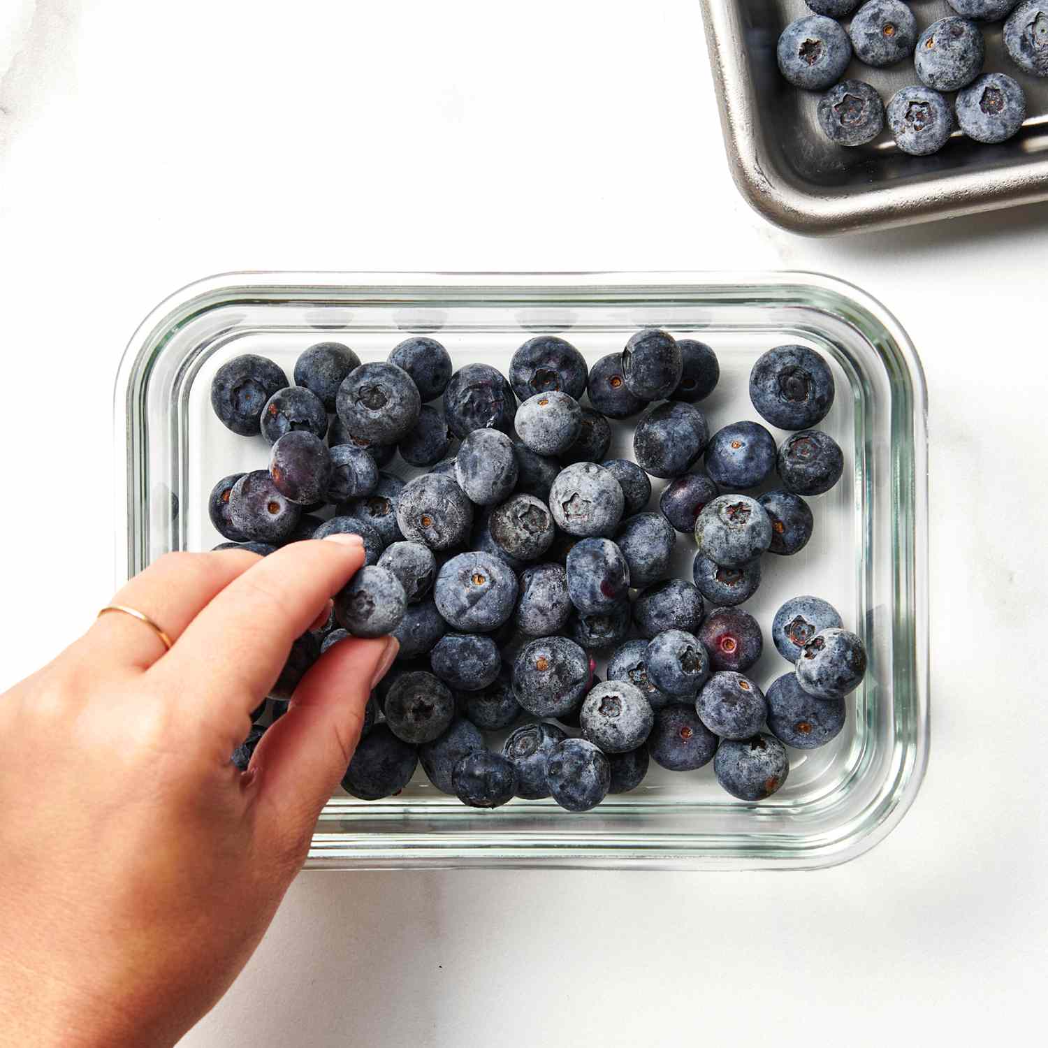 a hand placing a blueberry in a glass Tupperware
