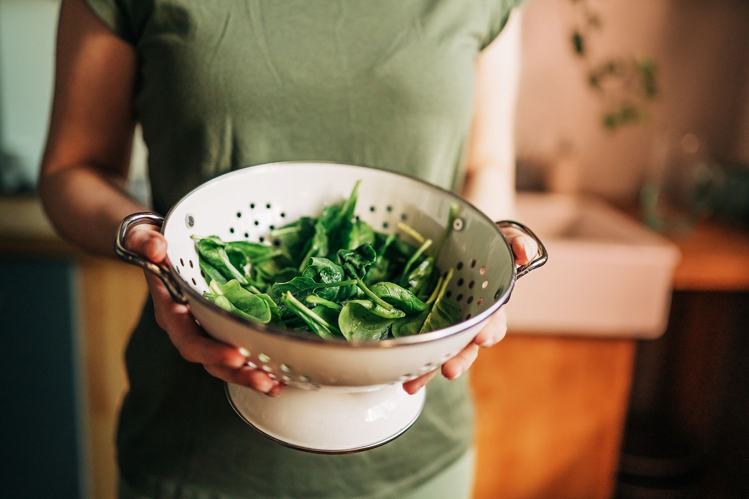 woman holding a colander with spinach
