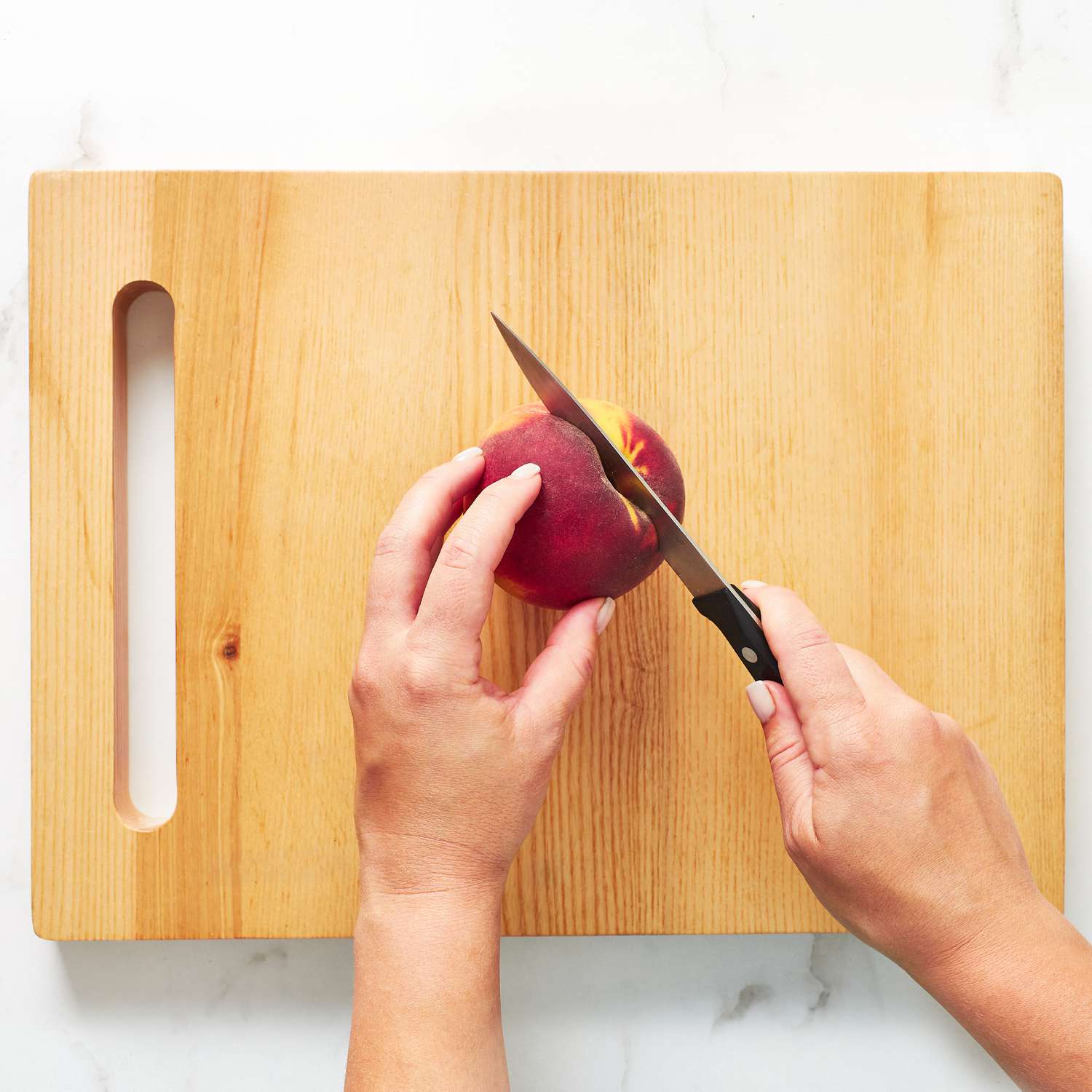 Close up on hands using a knife to cut a peach