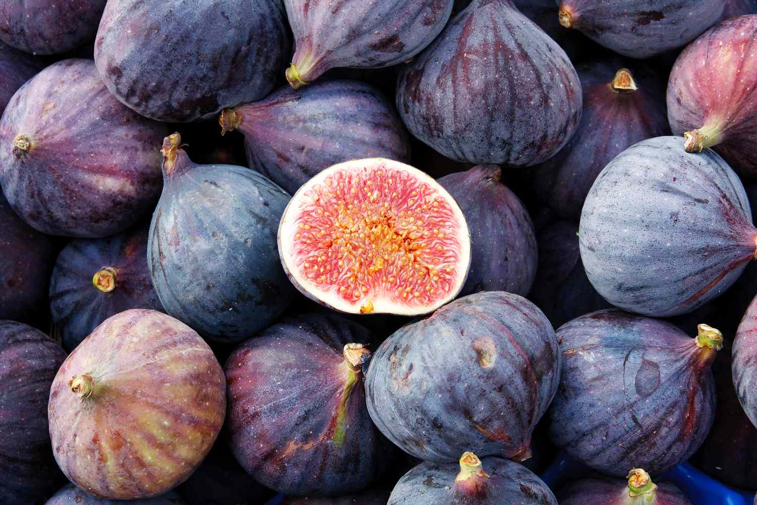 A close up shot of a pile of figs, one is cut open