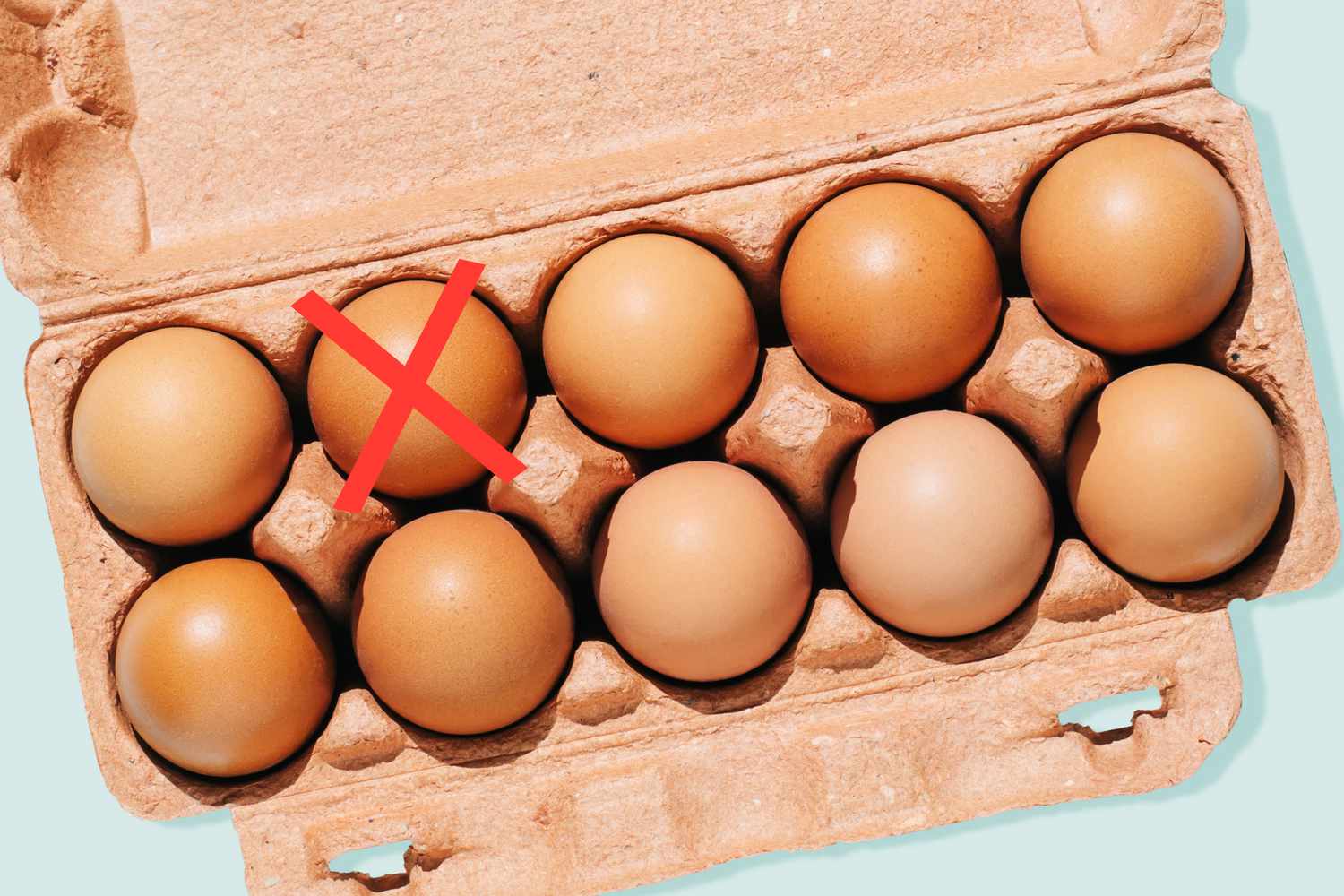 A carton of eggs on a blue background with a red X over one of the eggs